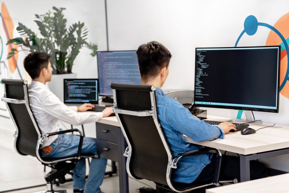 Dva programera za radnim stolovima programiraju u modernom uredu s velikim monitorima.