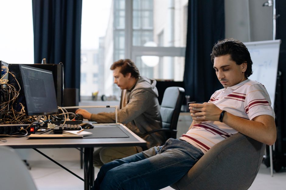 Dvojica muškaraca rade u modernom uredu, jedan na računalu, drugi na pametnom telefonu.